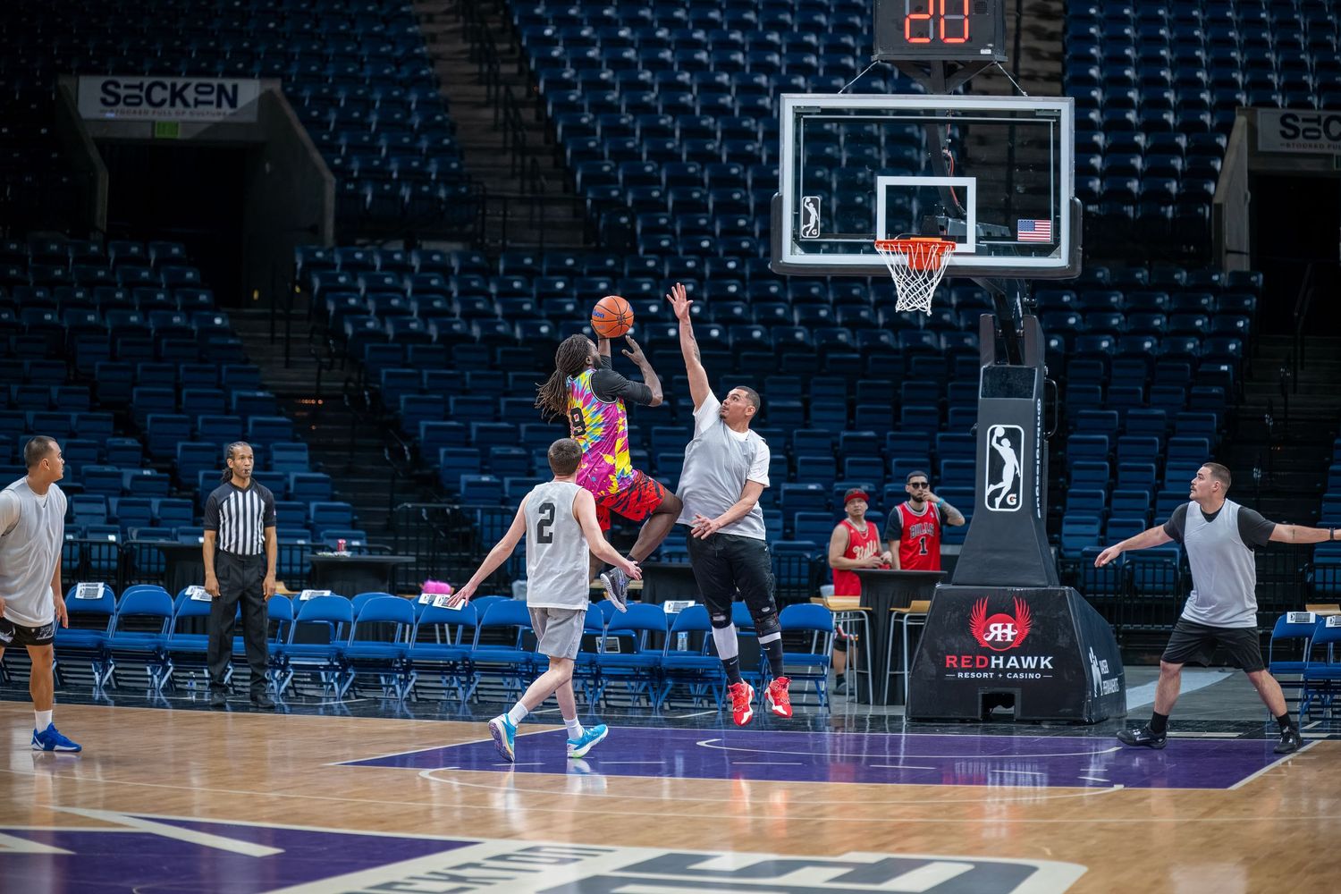 Basketball players practicing drills and shooting on a professional court with stadium seating in the background.