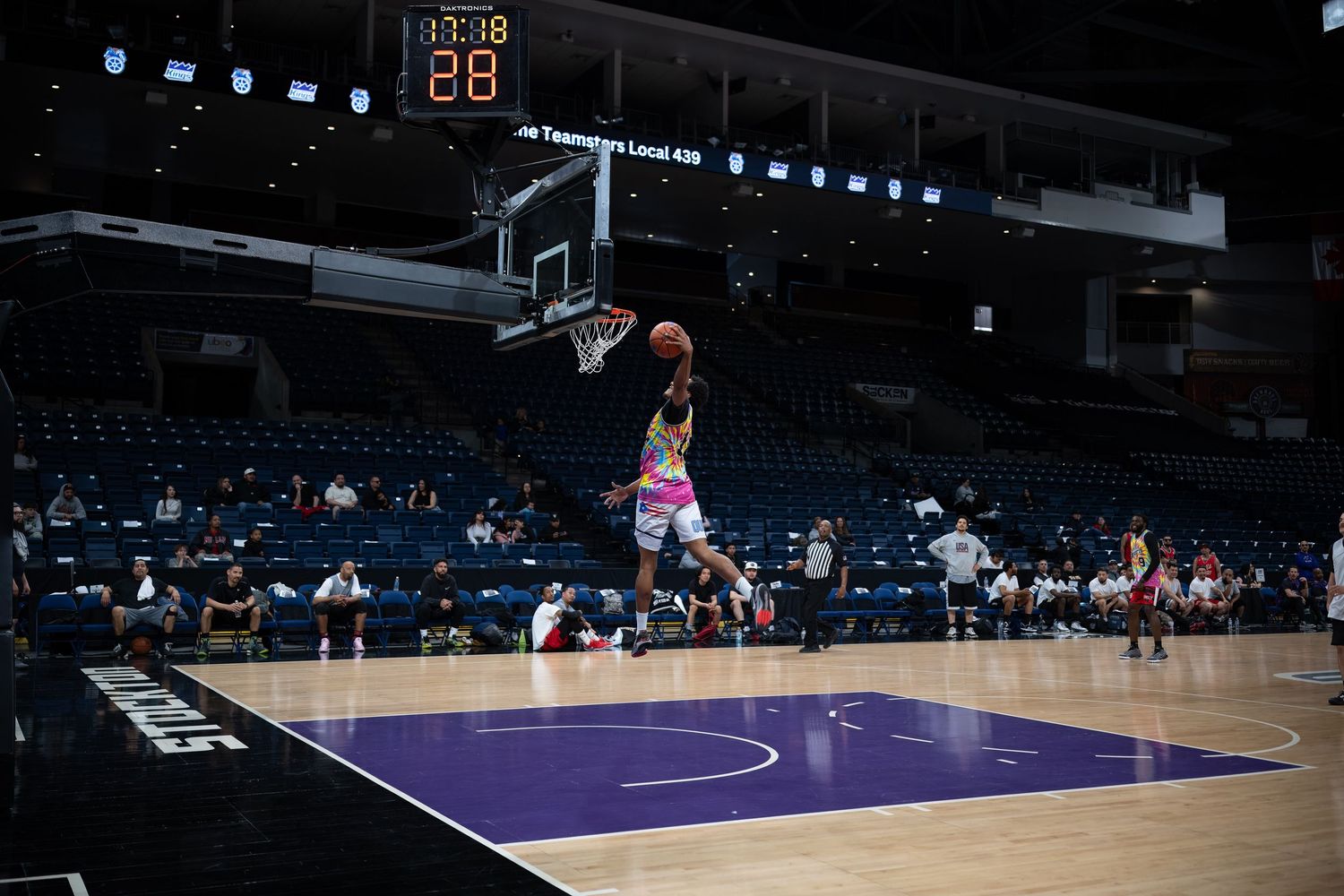 Basketball training session in an empty arena with players spread across the purple and white court.