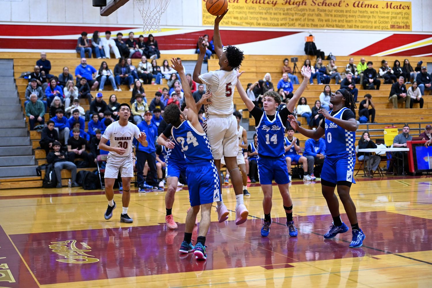 Players battle for position during a high school basketball game with spectators watching.