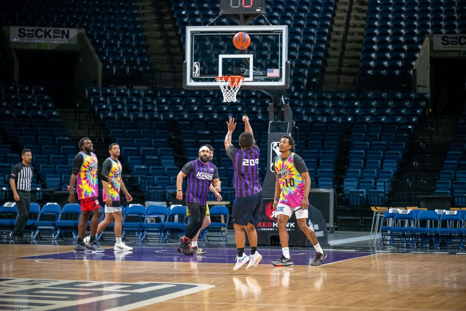 Wide view of basketball practice in an arena showing multiple players and coaches on court.