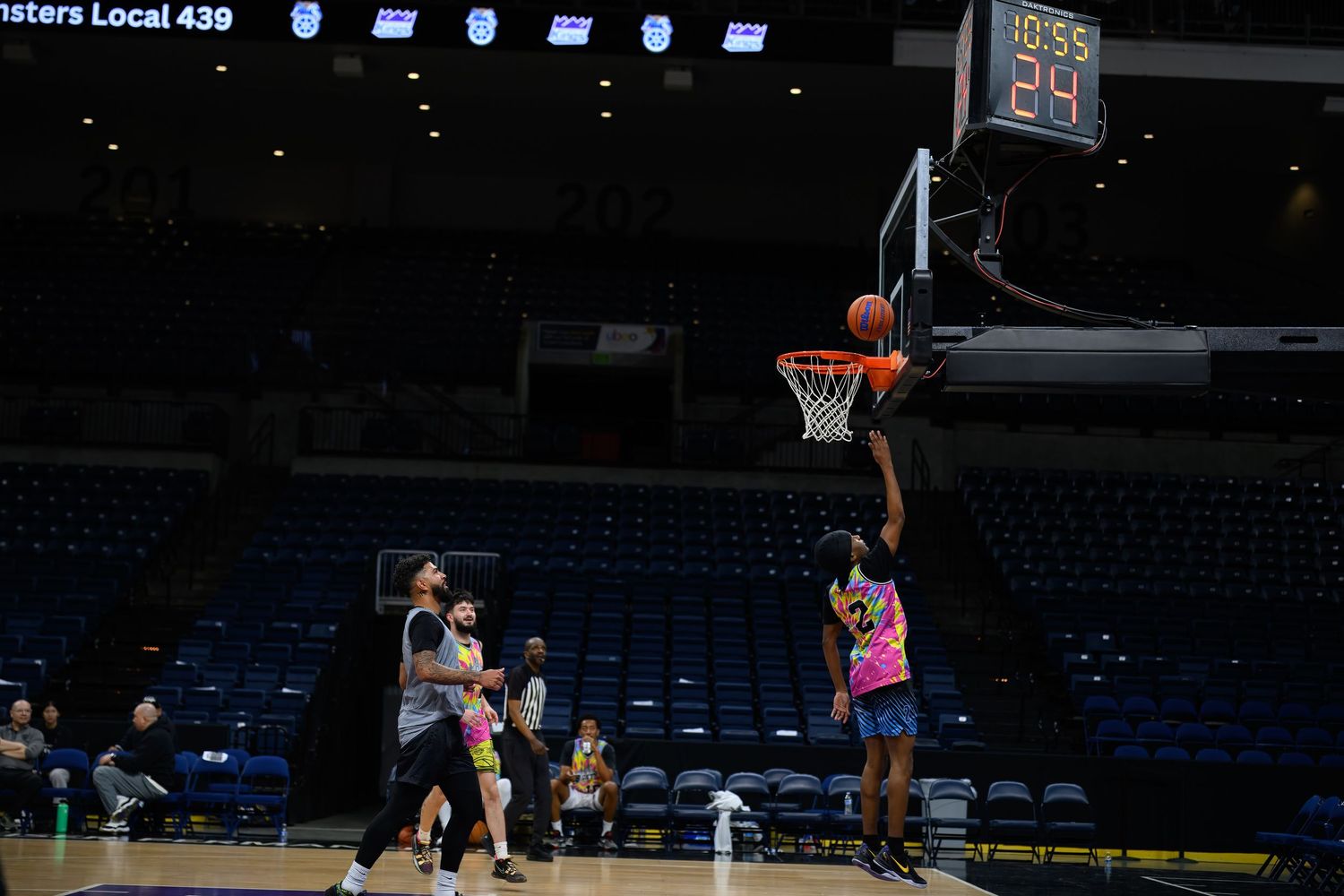 Basketball players compete in an empty arena with one athlete attempting a shot near the basket.