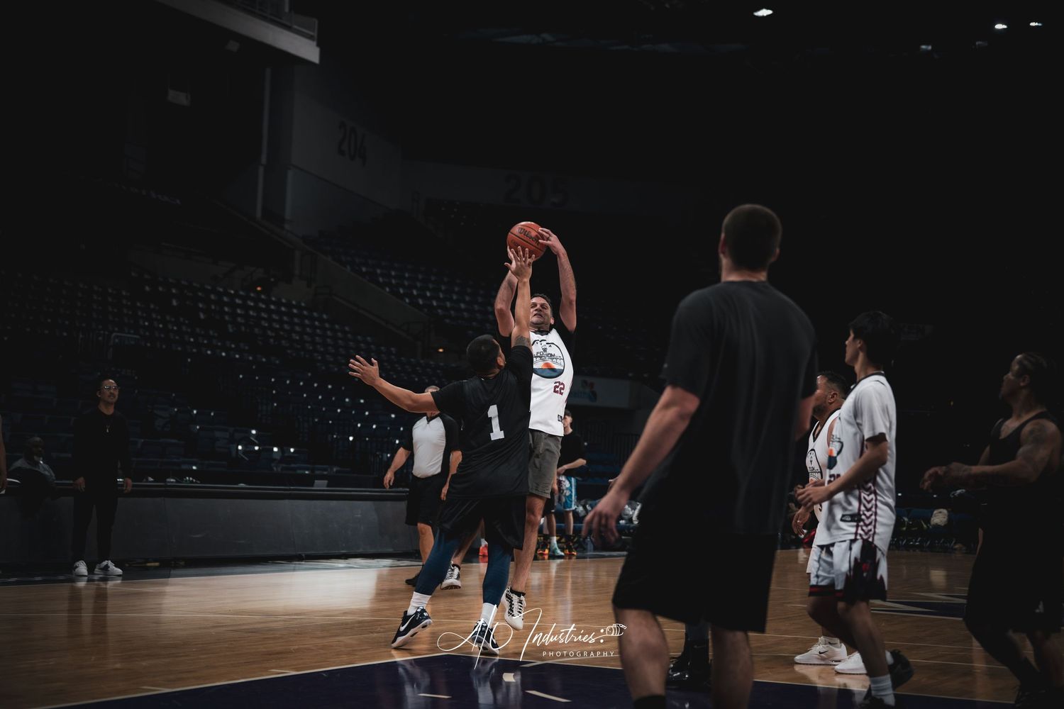 Basketball player wearing number 1 jersey takes jump shot during indoor arena practice game with defenders.