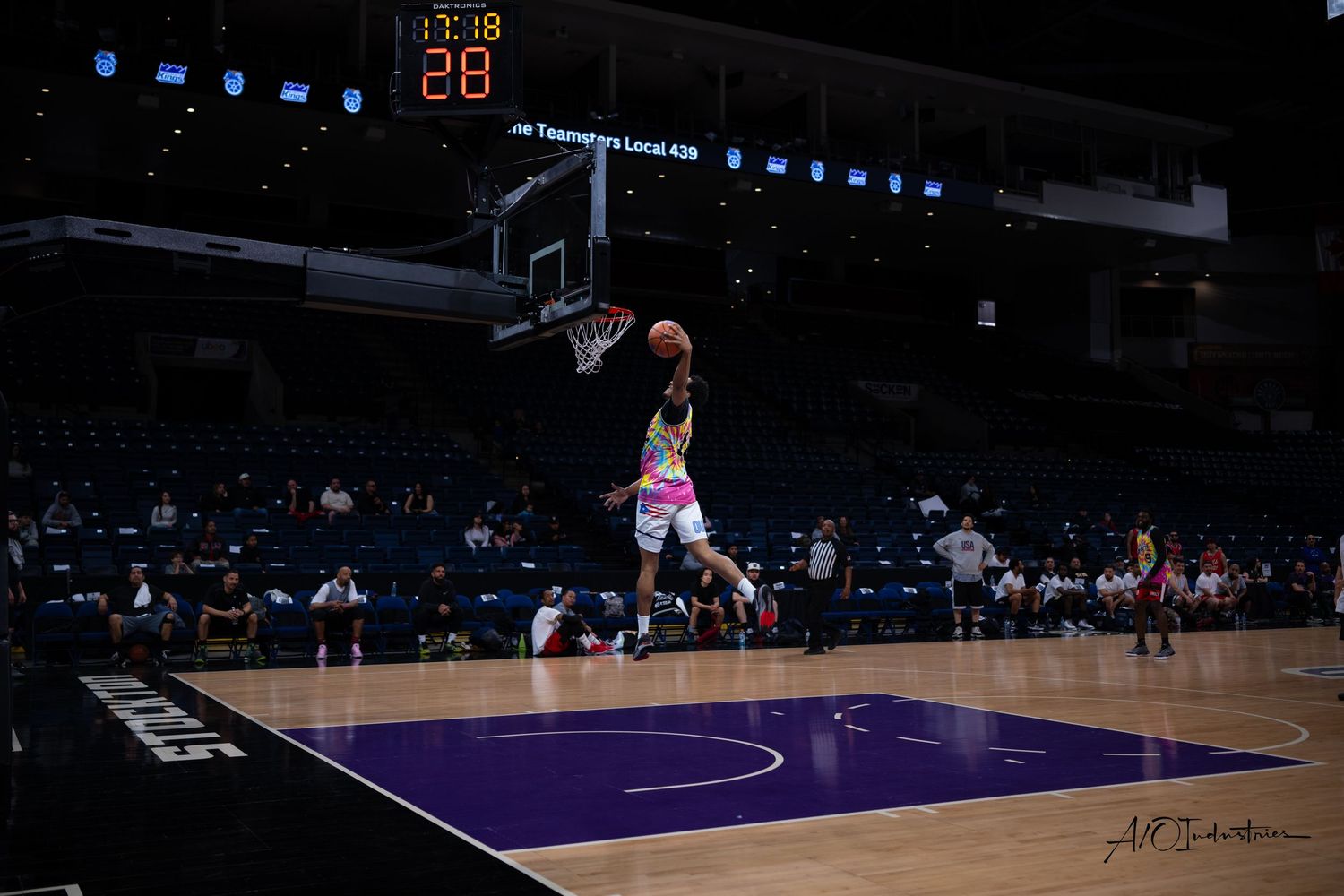 Basketball player soars through the air for a dramatic dunk on a purple court.