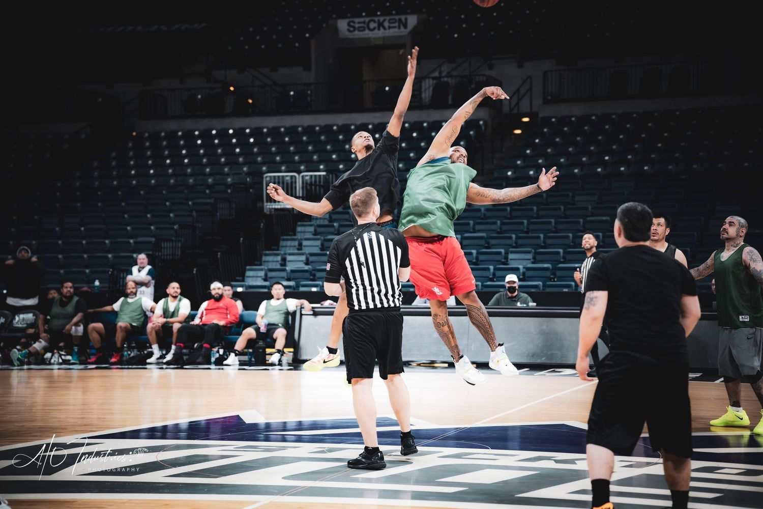 Two players contest a jump ball as a referee watches during an indoor basketball game.