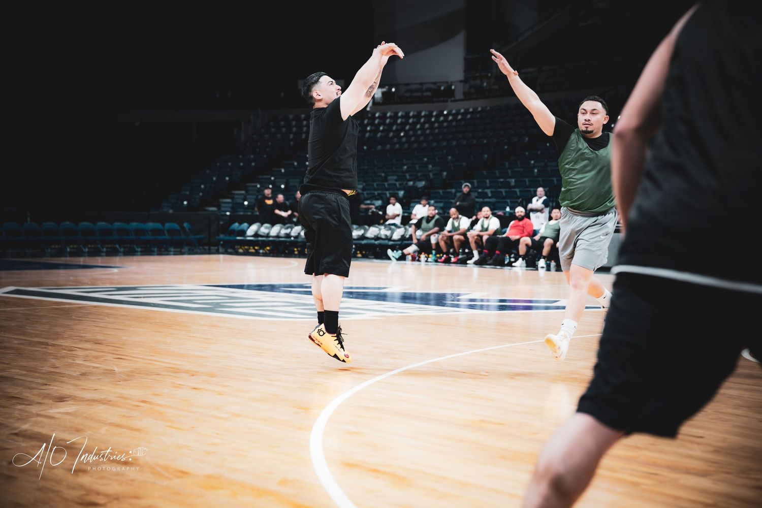 A basketball player releases a jump shot while a defender contests near the baseline.