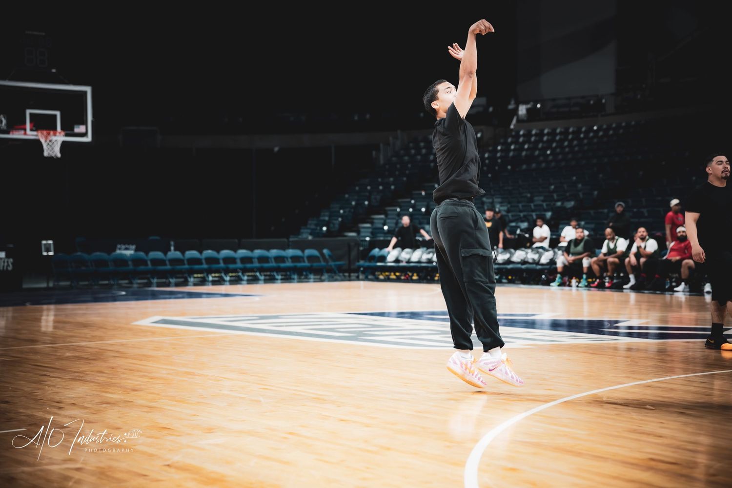 A basketball player shoots a jump shot alone on an indoor court during practice in a dark arena.
