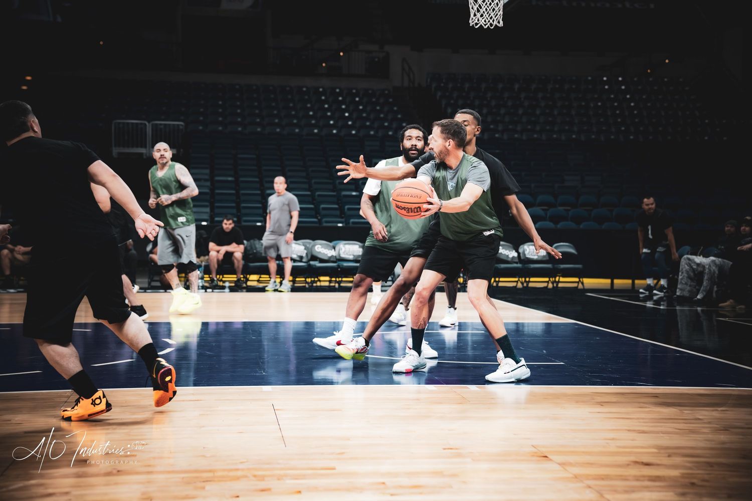Basketball players compete for the ball during an indoor practice session on a hardwood court in an arena.