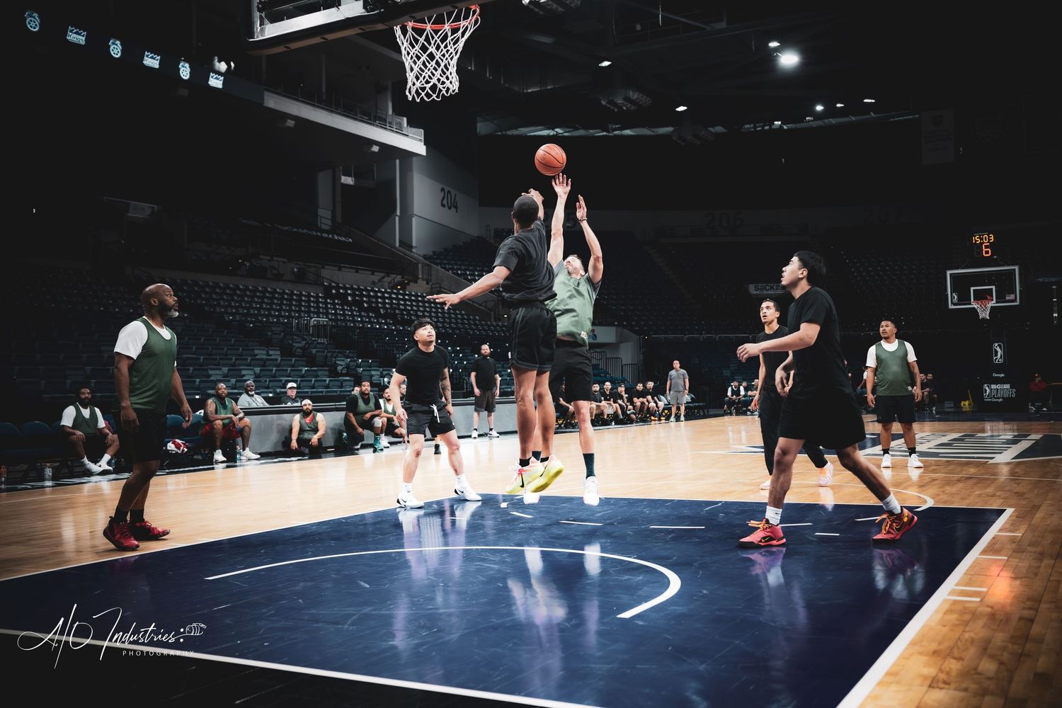 Basketball players compete in a layup drill during an indoor arena practice session under bright court lights.