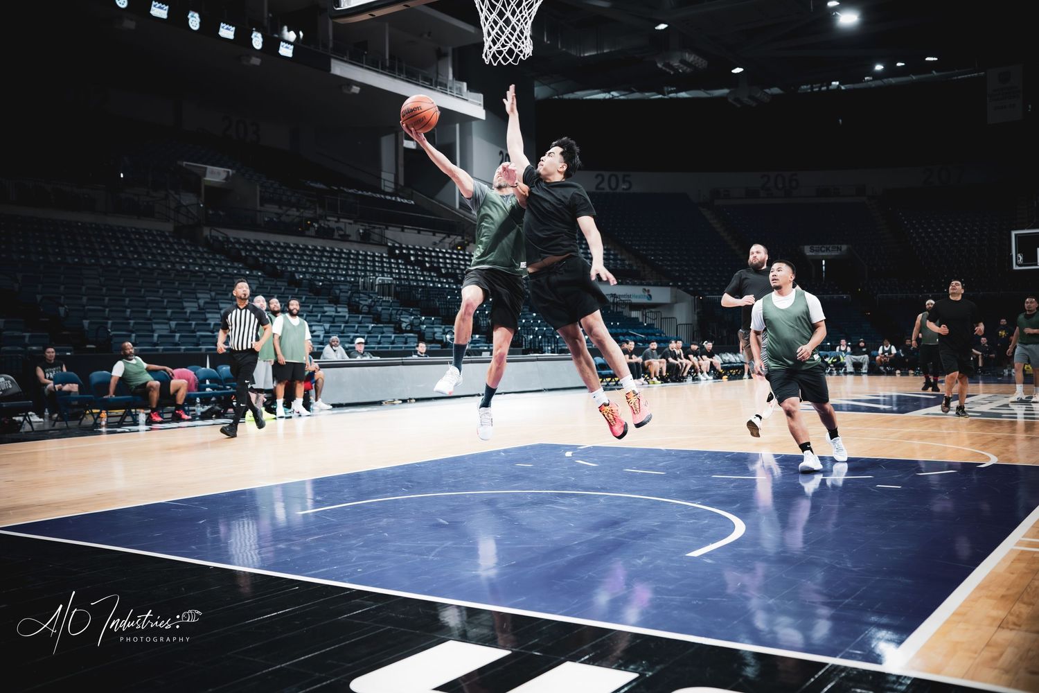 Basketball player leaps for a dramatic layup during an indoor arena practice session with teammates watching.