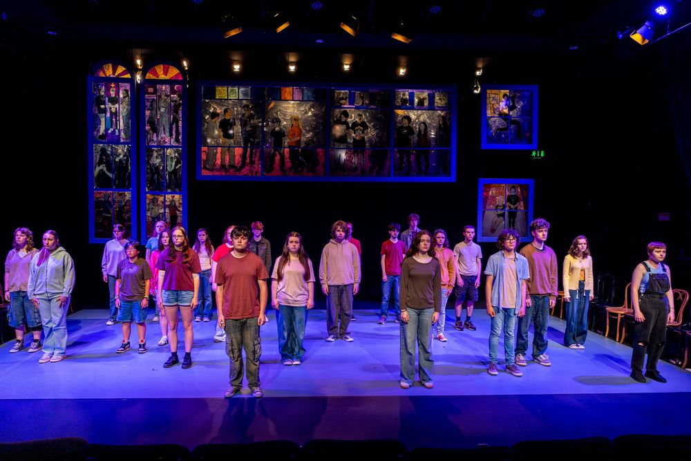 Stage performers stand in formation during a theatrical production with dramatic blue lighting and set design.