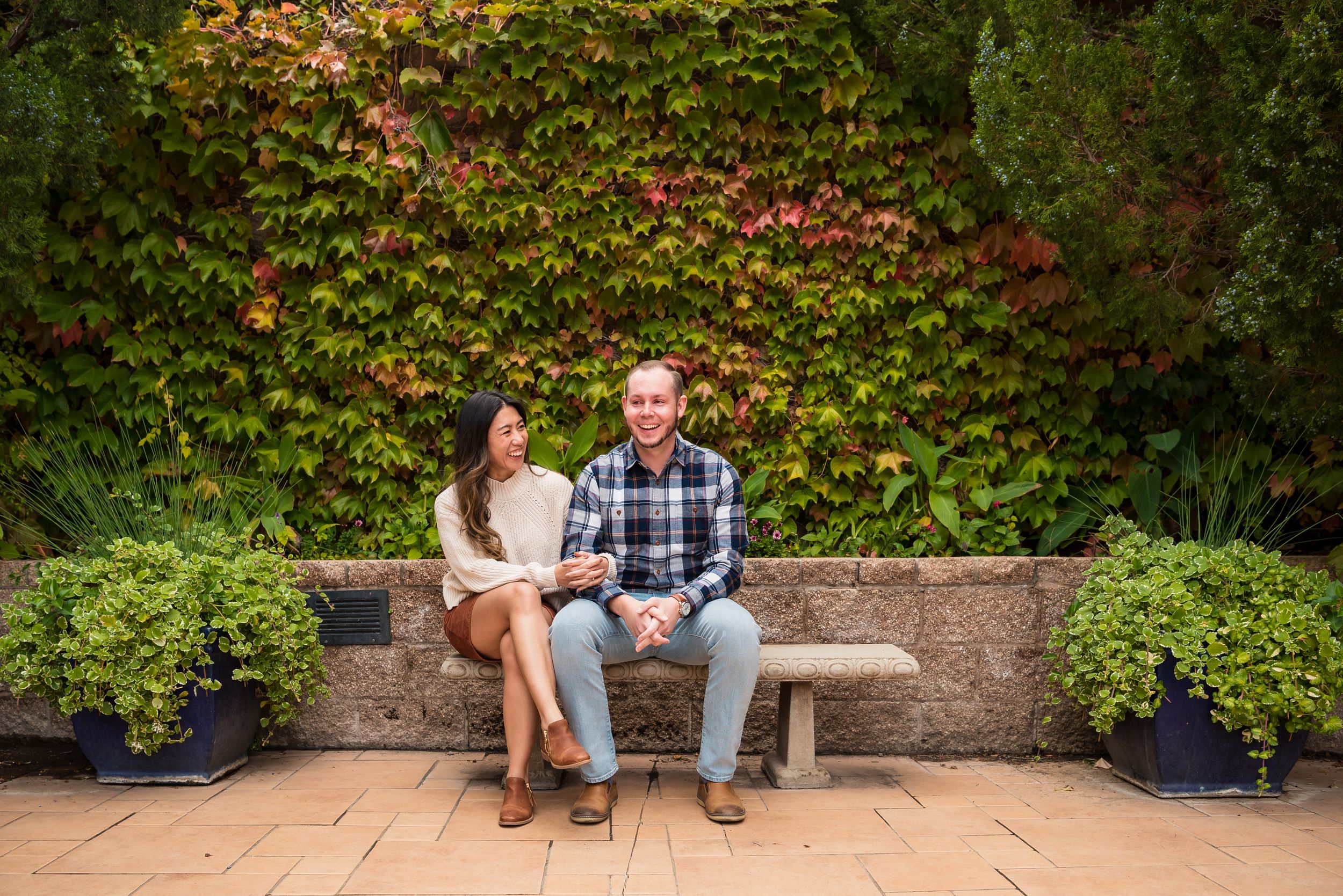 A couple sitting on a stone bench with ivy covered wall in a garden setting at sunset.