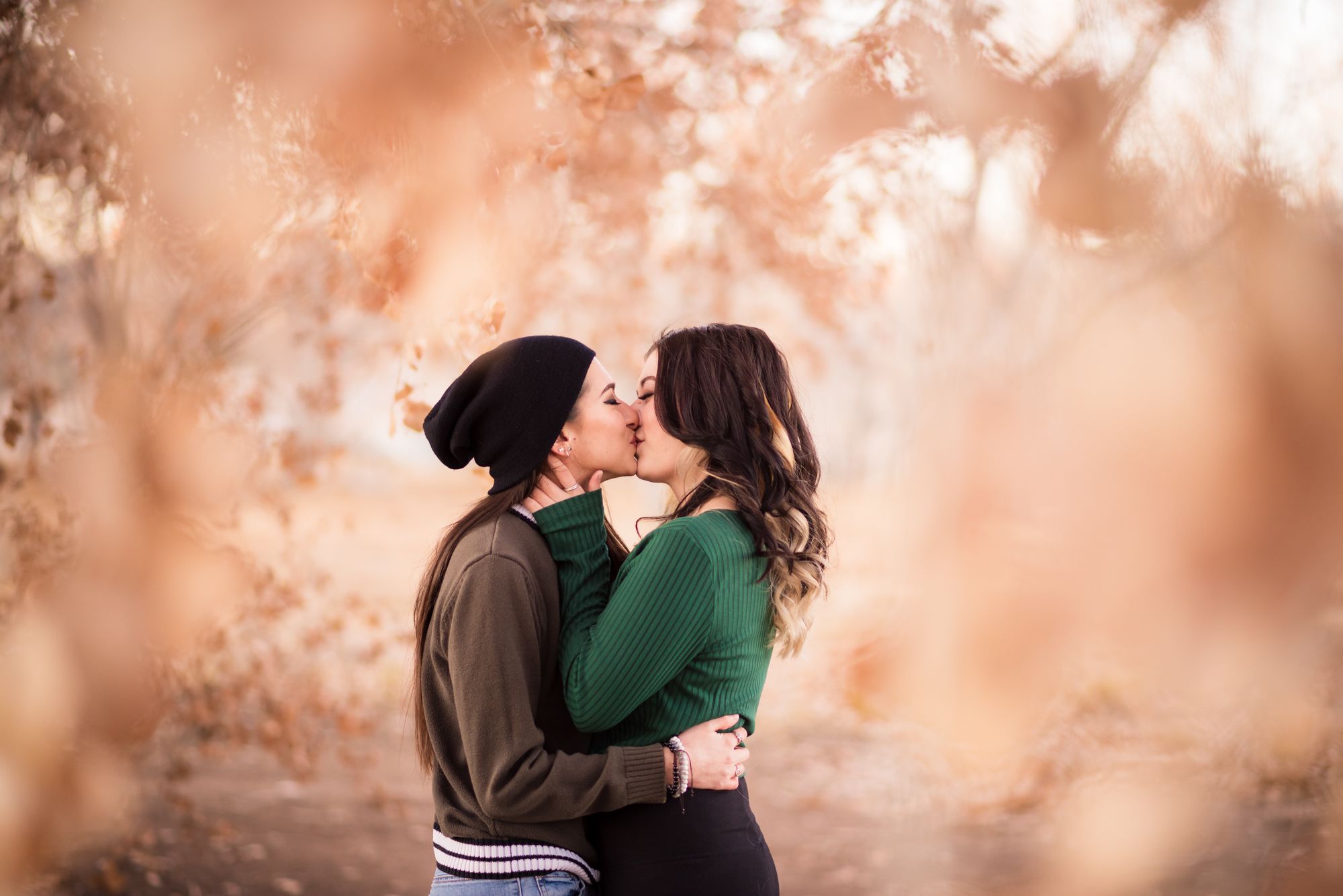 A romantic couple embraces and kisses in a dreamy outdoor setting with soft peachy bokeh lighting effects.