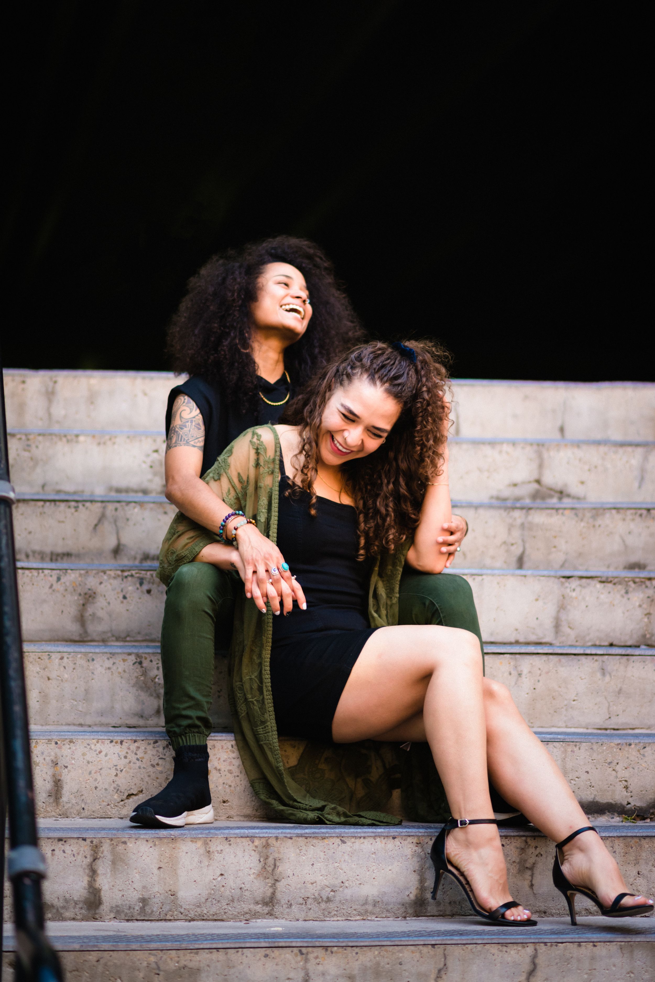 Two people in stylish casual outfits relax on concrete steps in a candid urban photo shoot.