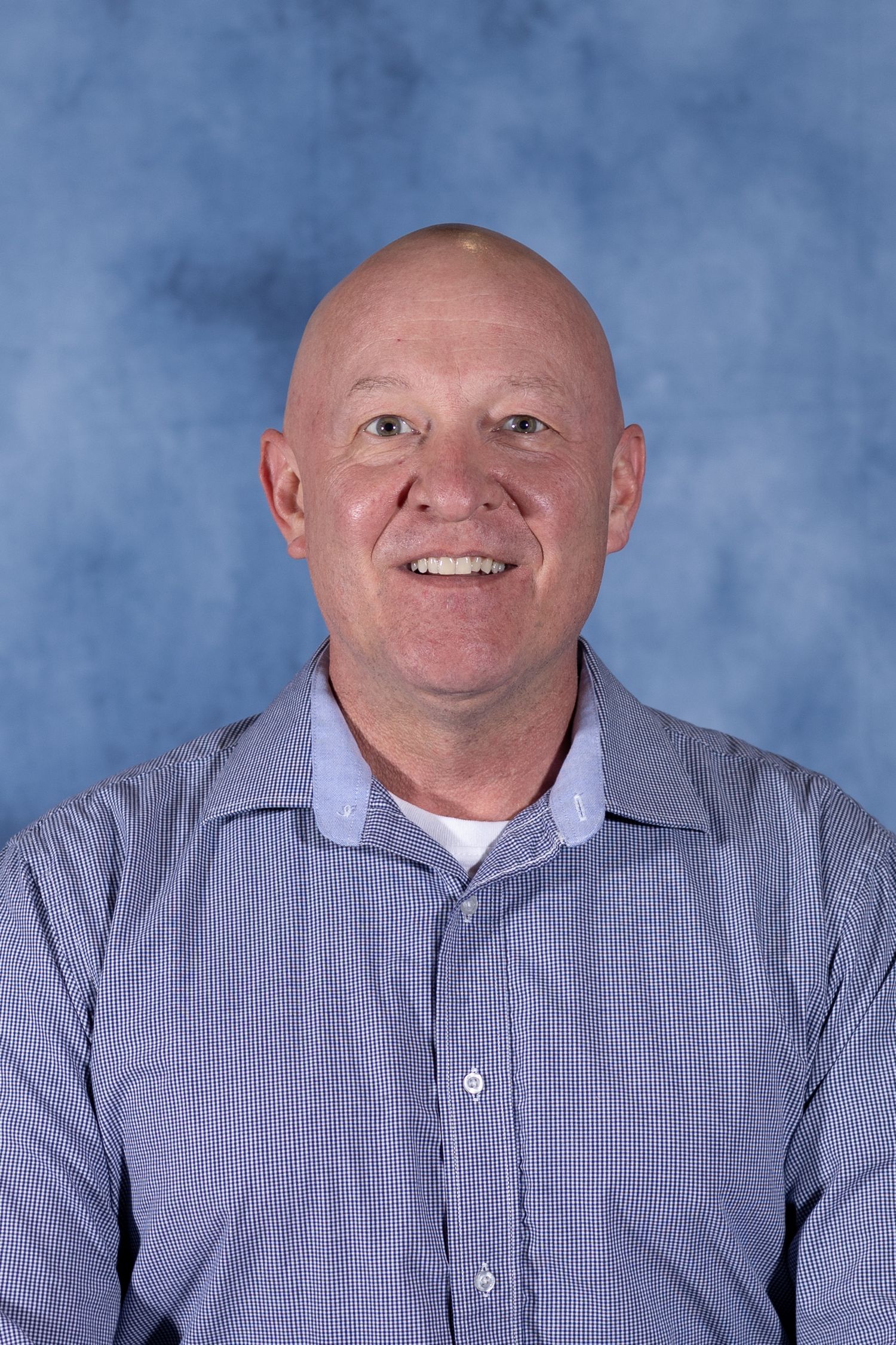 Professional headshot portrait of person in blue checkered shirt against mottled blue background.