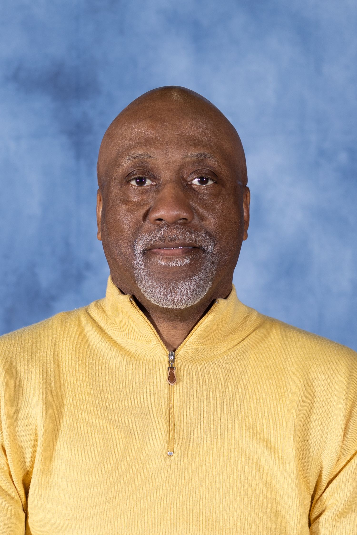 Professional portrait photo of a person wearing a yellow quarter-zip pullover against a blue background.