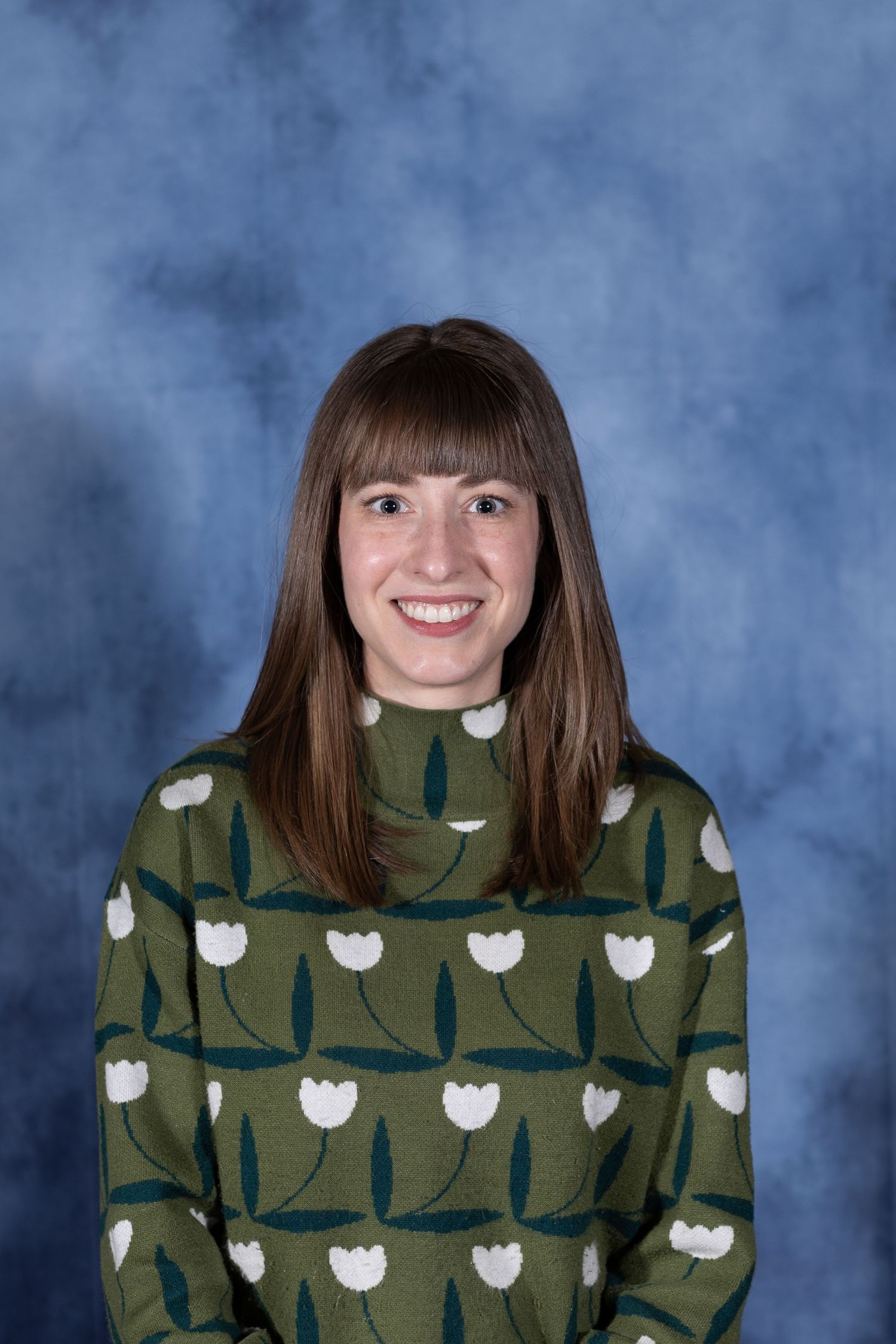 Studio portrait against blue background showing person wearing green sweater with white tulip pattern.