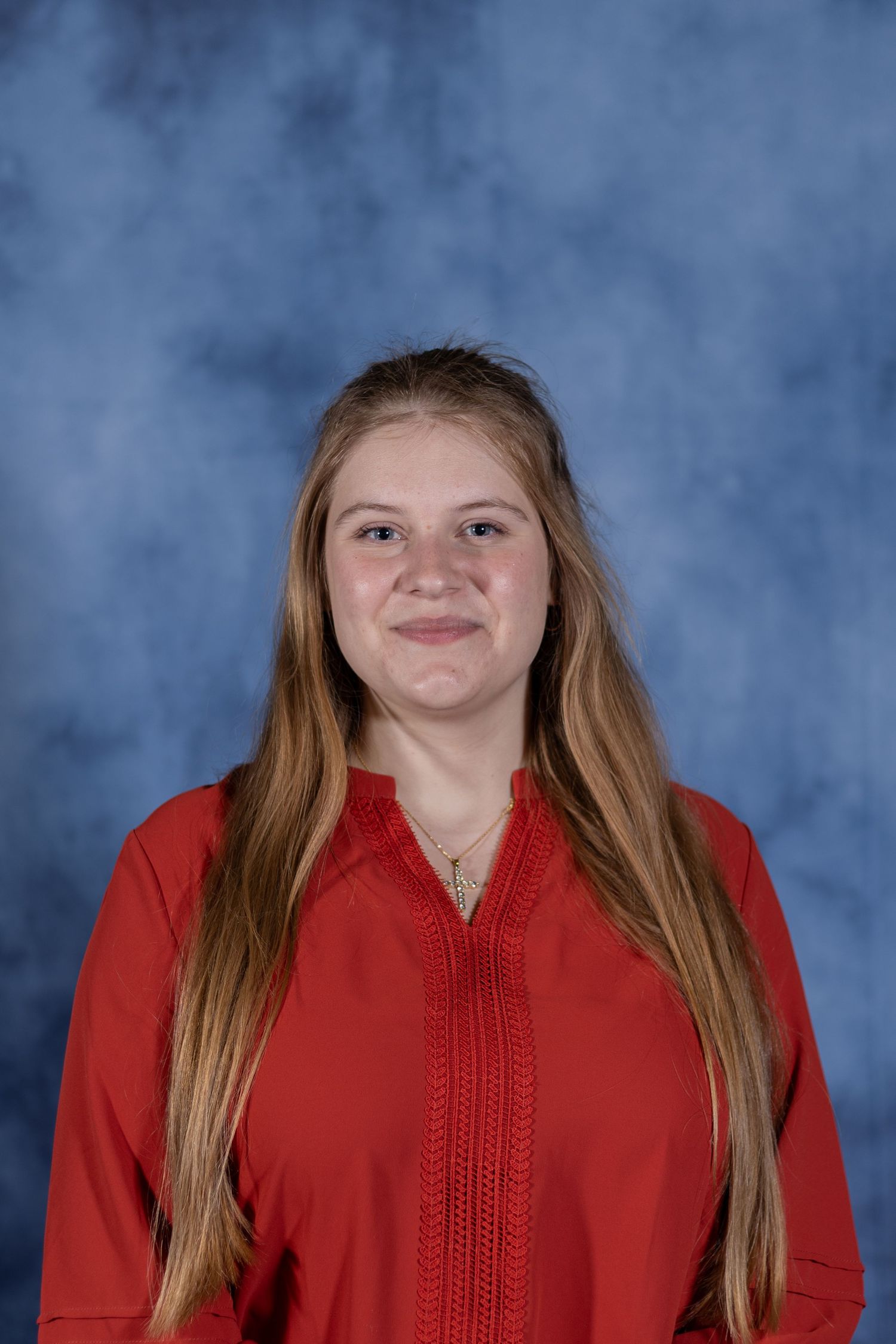 Student portrait against blue mottled backdrop wearing long red top with detailed neckline and long hair.