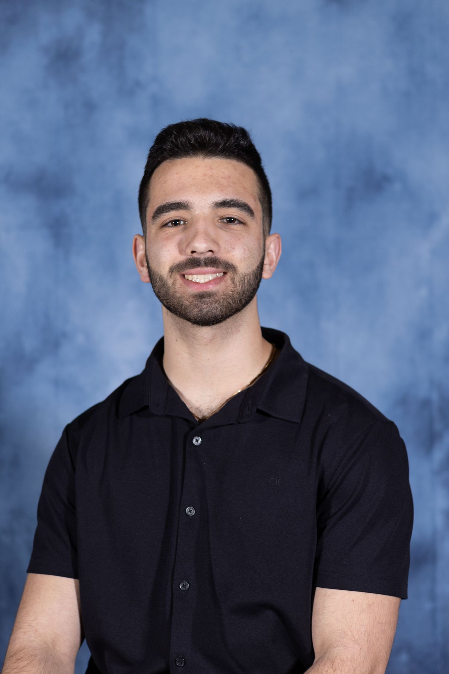 Professional headshot portrait of someone wearing a black polo shirt against a mottled blue backdrop.
