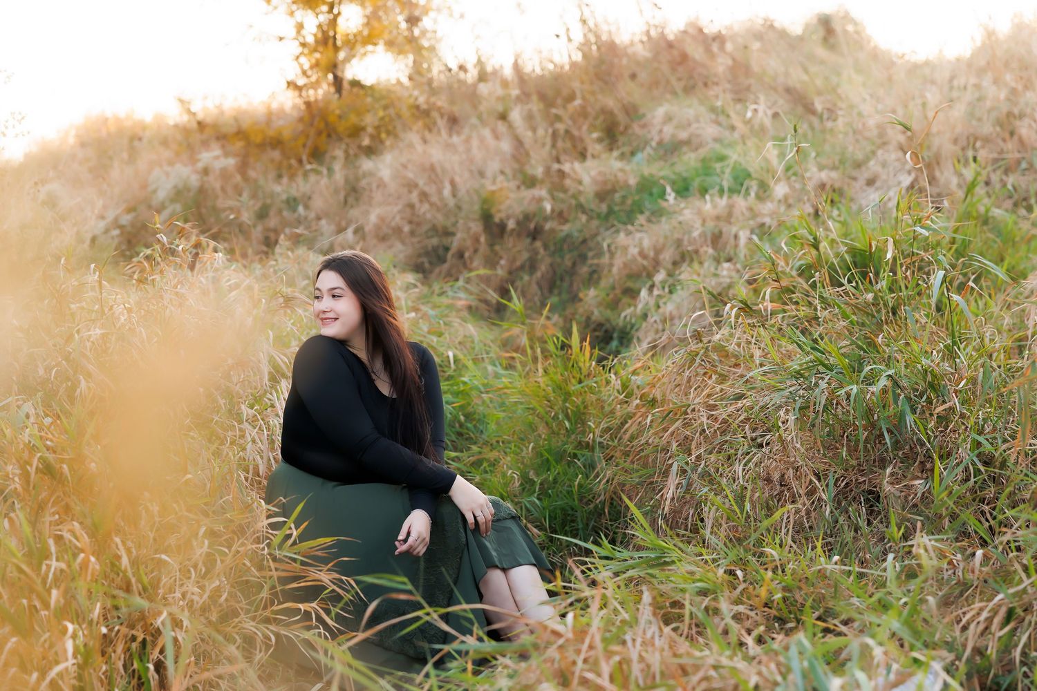 Young person in a flowing white dress with long sleeves poses outdoors during golden hour sunset.