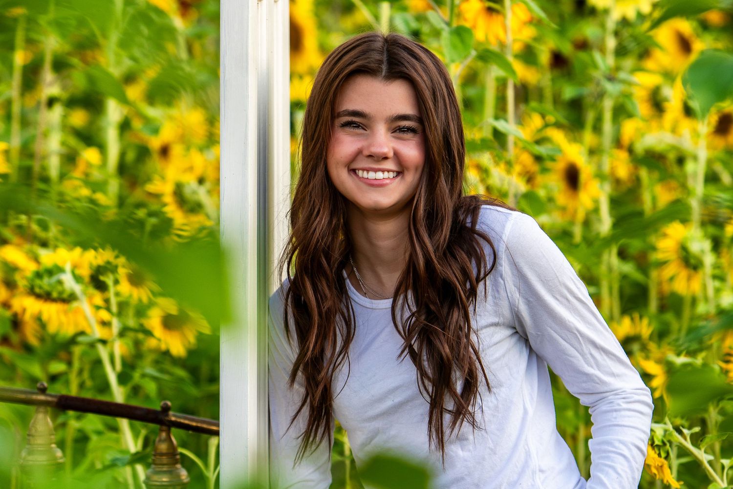 Long brown hair and white shirt against vibrant yellow wildflowers in a summer garden setting.