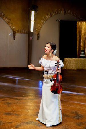 A performer in white plays violin on a rustic indoor stage.