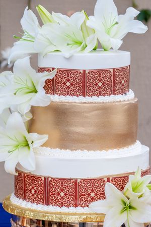 Elegant tiered wedding cake decorated with white lilies and copper metallic details.