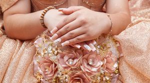 Close-up of hands adorned with jewelry against a rose gold sequined fabric background.