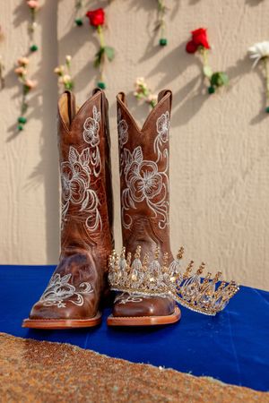 Brown leather cowboy boots with white embroidery displayed next to ornate crowns on blue fabric.