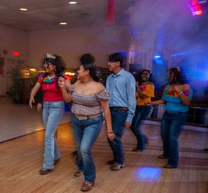 Line dancers in jeans perform synchronized steps on a dance floor with colorful lighting.