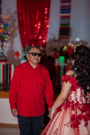 Dancers in red and black formal attire perform at a festive event with decorative lighting.