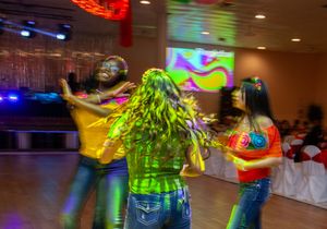 Dancers in colorful outfits move energetically under disco lights at a festive indoor party.