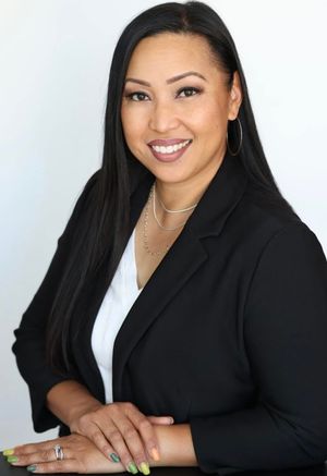 Professional headshot of someone in a black blazer and white top smiling warmly against a light background.