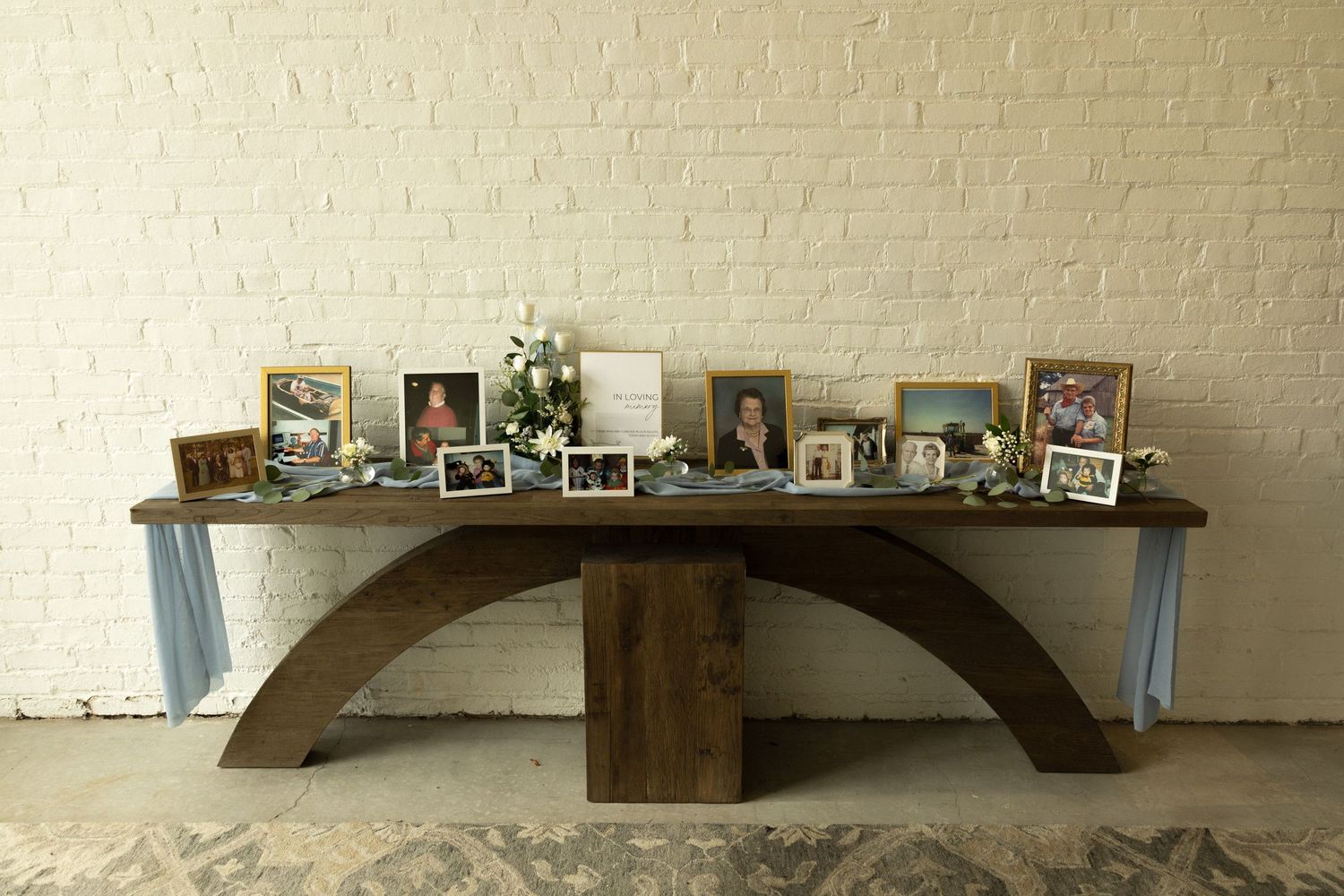 A curved wooden shelf displaying framed photos and memorabilia against a white brick wall.