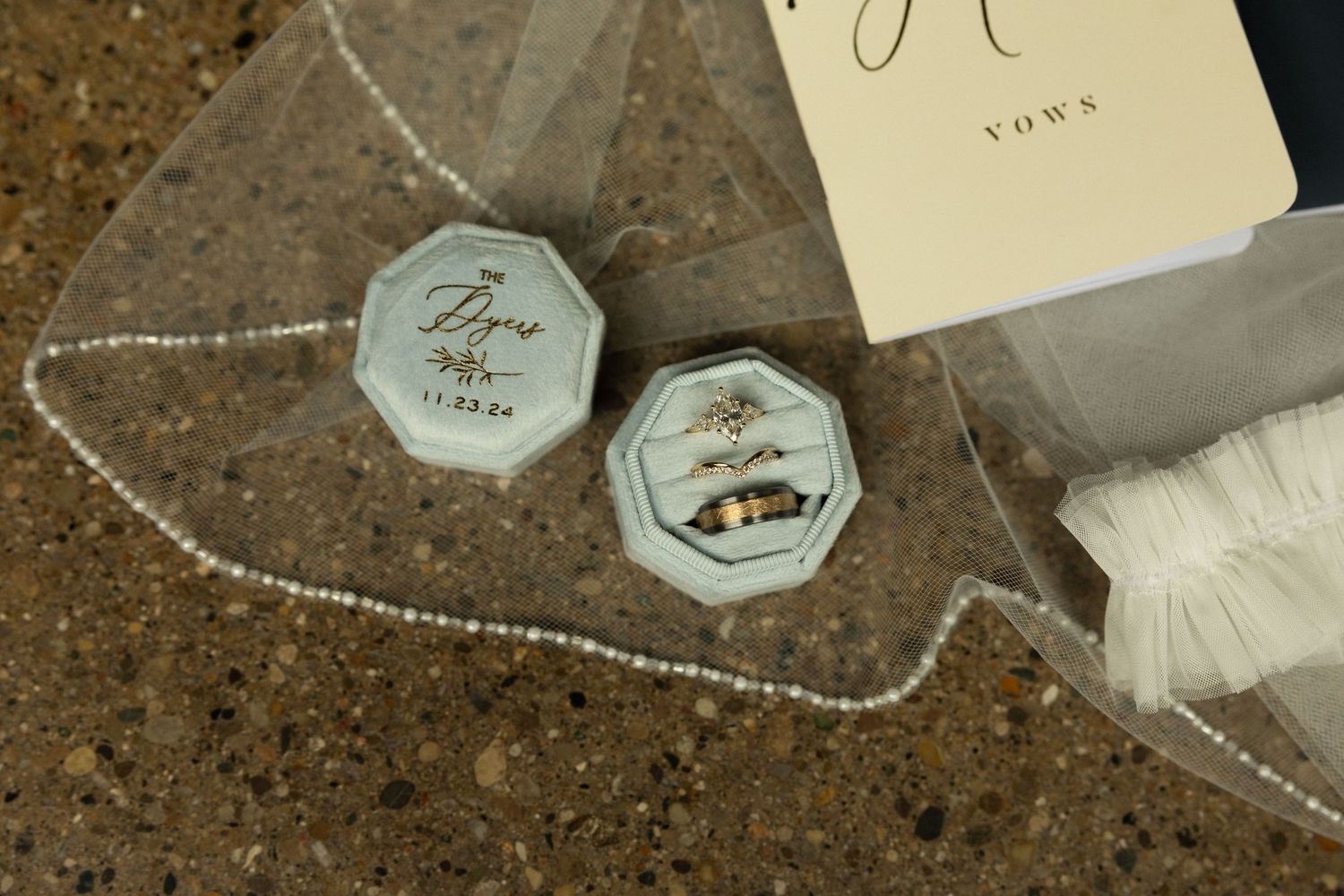Close-up of hexagonal ring boxes and veil on textured surface.