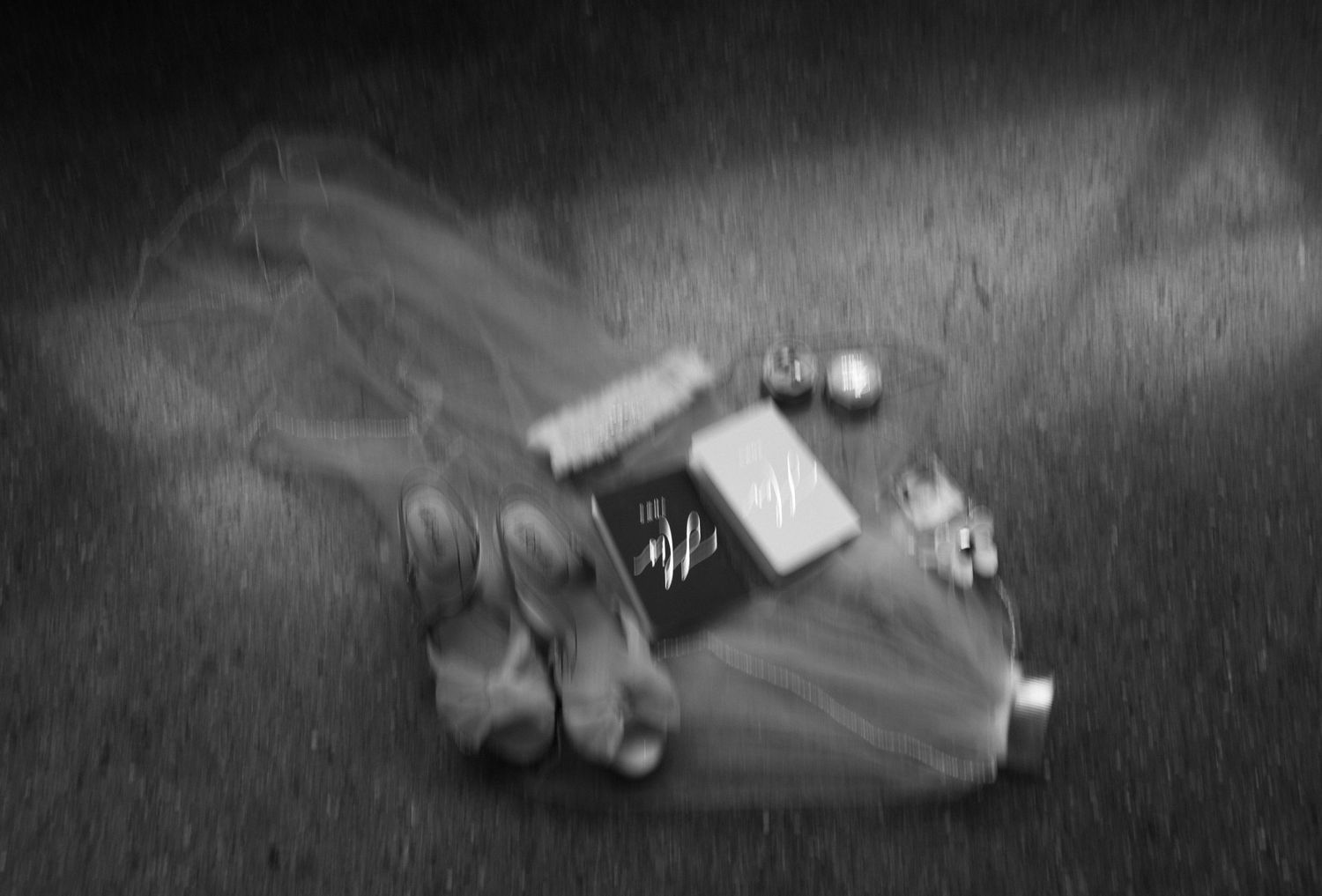 Black and white photo of wedding accessories arranged on ground.