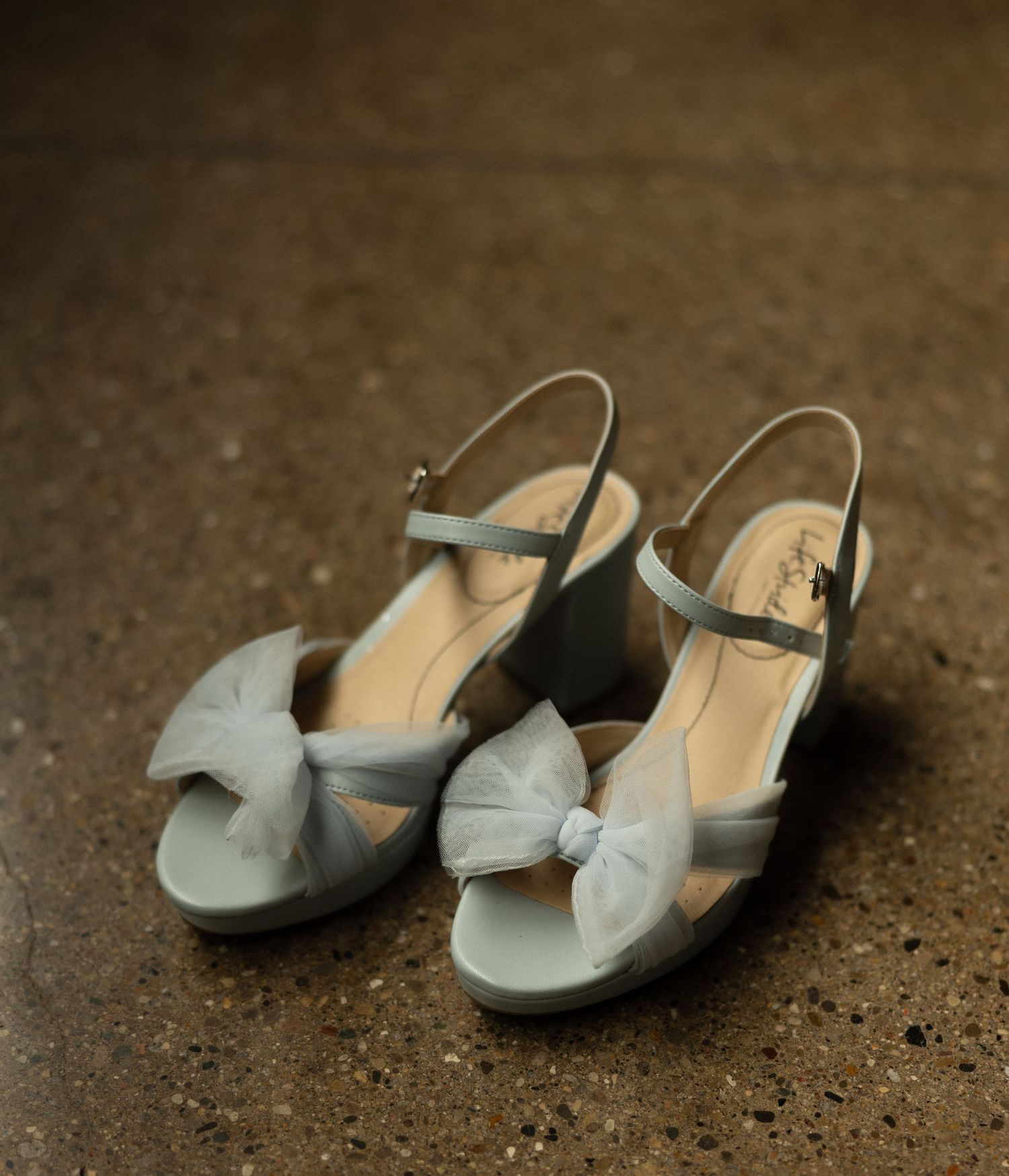 Pale blue wedding shoes with bow details on concrete surface.