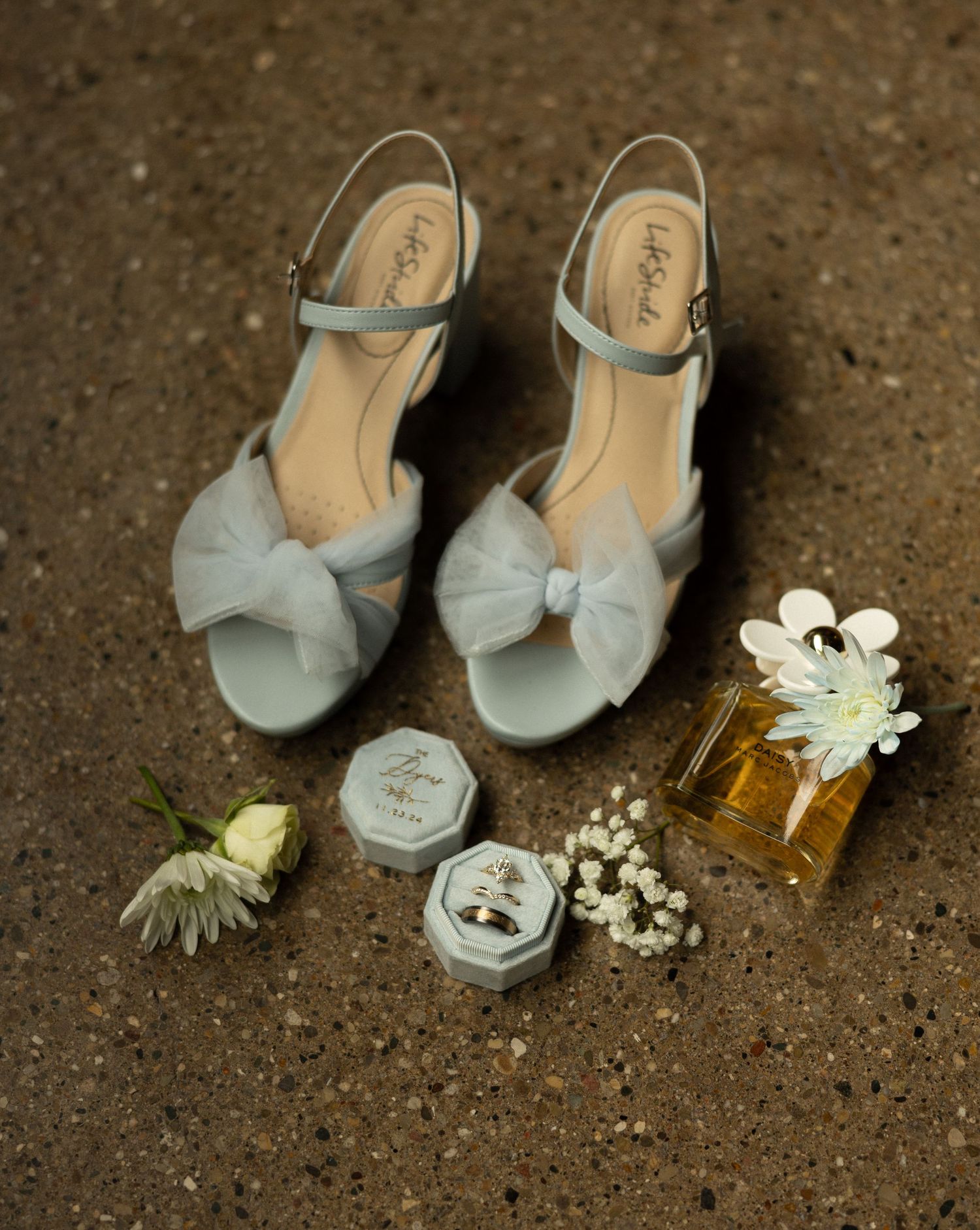 Vintage-style blue wedding shoes with perfume bottle and ring boxes on concrete floor.