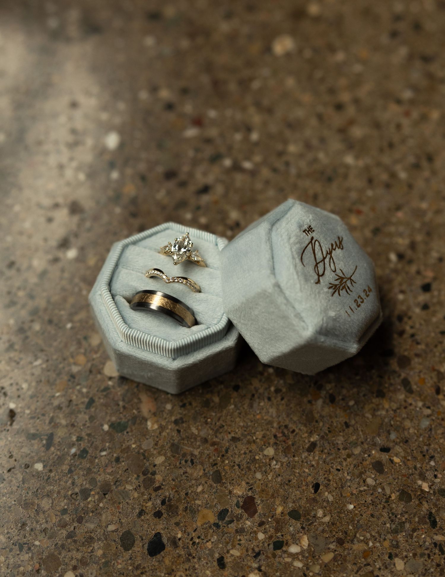 Two hexagonal ring boxes containing wedding bands on textured concrete surface.