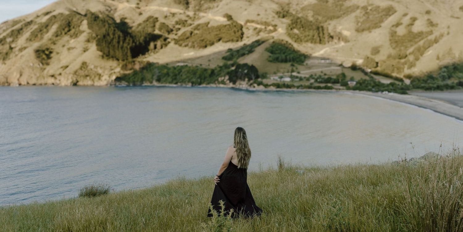 Silhouette of person overlooking coastal bay and rolling hills.
