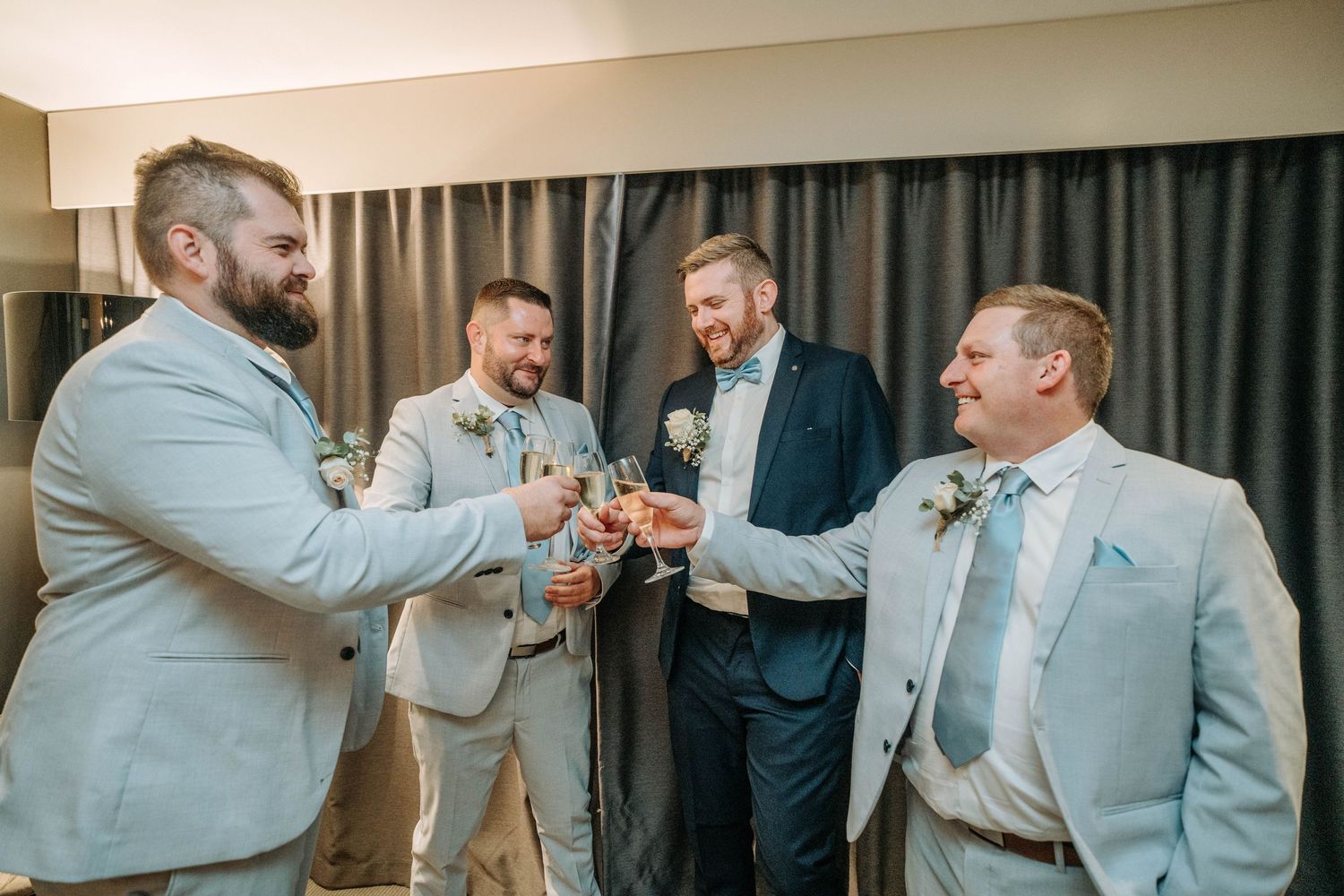 Groomsmen in light colored suits share drinks and laughs before the ceremony.