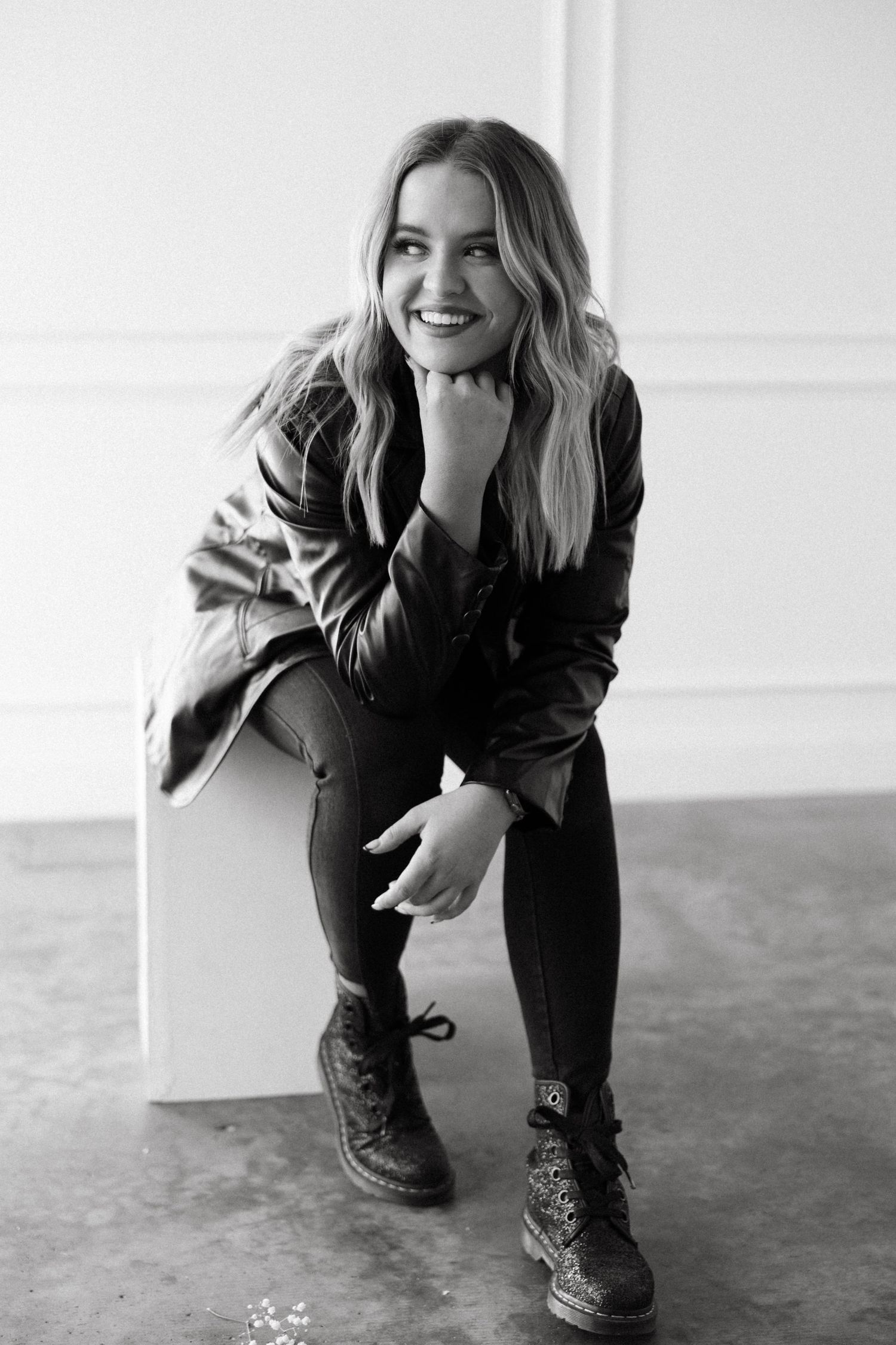 A black and white portrait of someone in leather jacket and boots sitting on a white cube.
