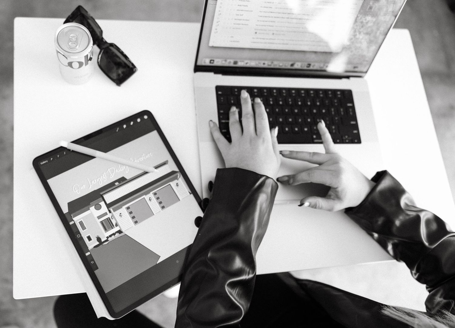 Top view of hands typing on laptop with tablet showing website layout on desk.