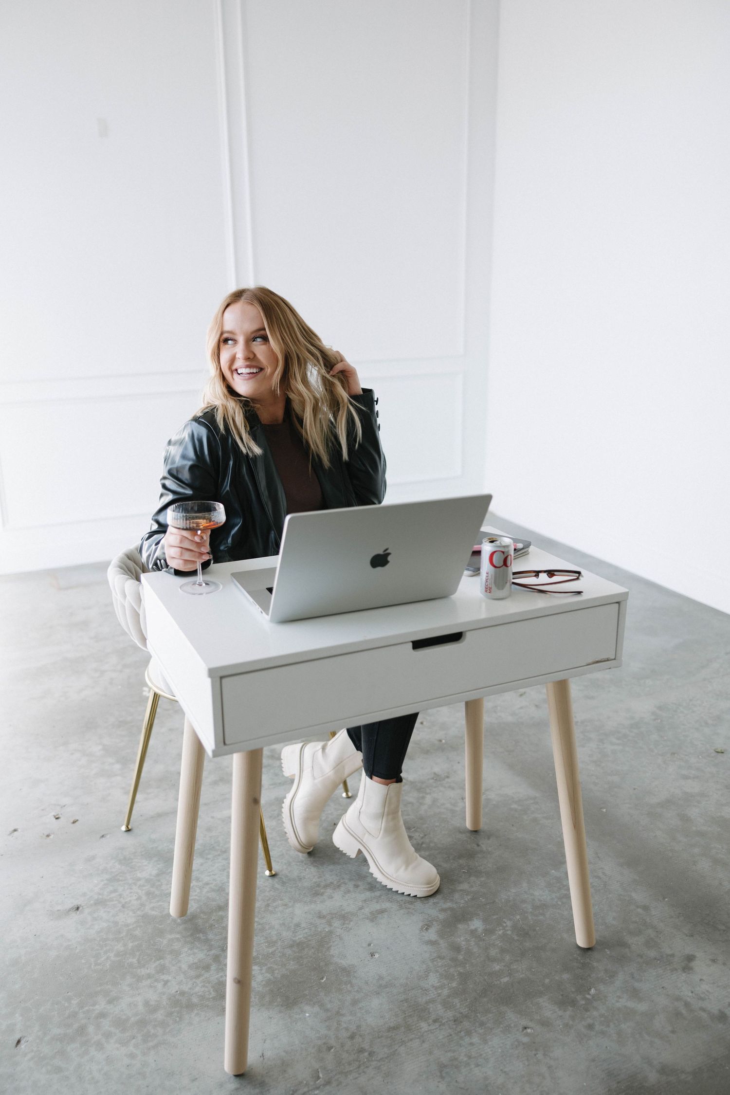 Person in black jacket works on MacBook at minimalist white desk with coffee.