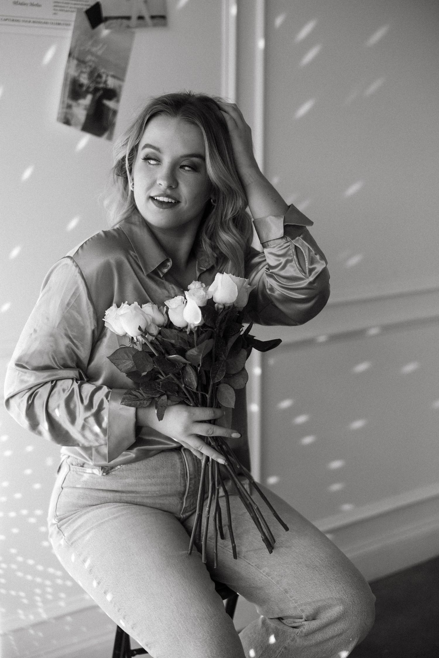 Black and white portrait of person holding white flowers in casual setting with dramatic lighting.