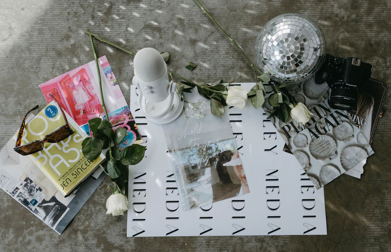 Flatlay arrangement of books, camera, disco ball and decorative items on a light surface.