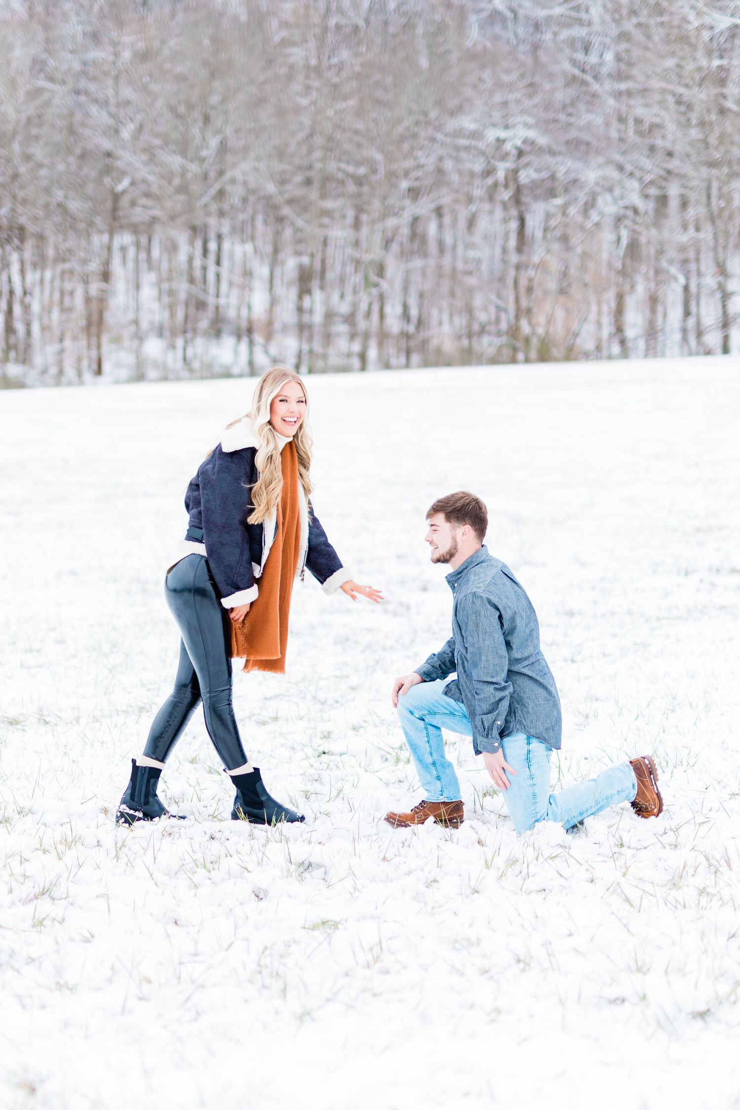 A surprise proposal moment captured in a snow-covered field with winter trees in background.