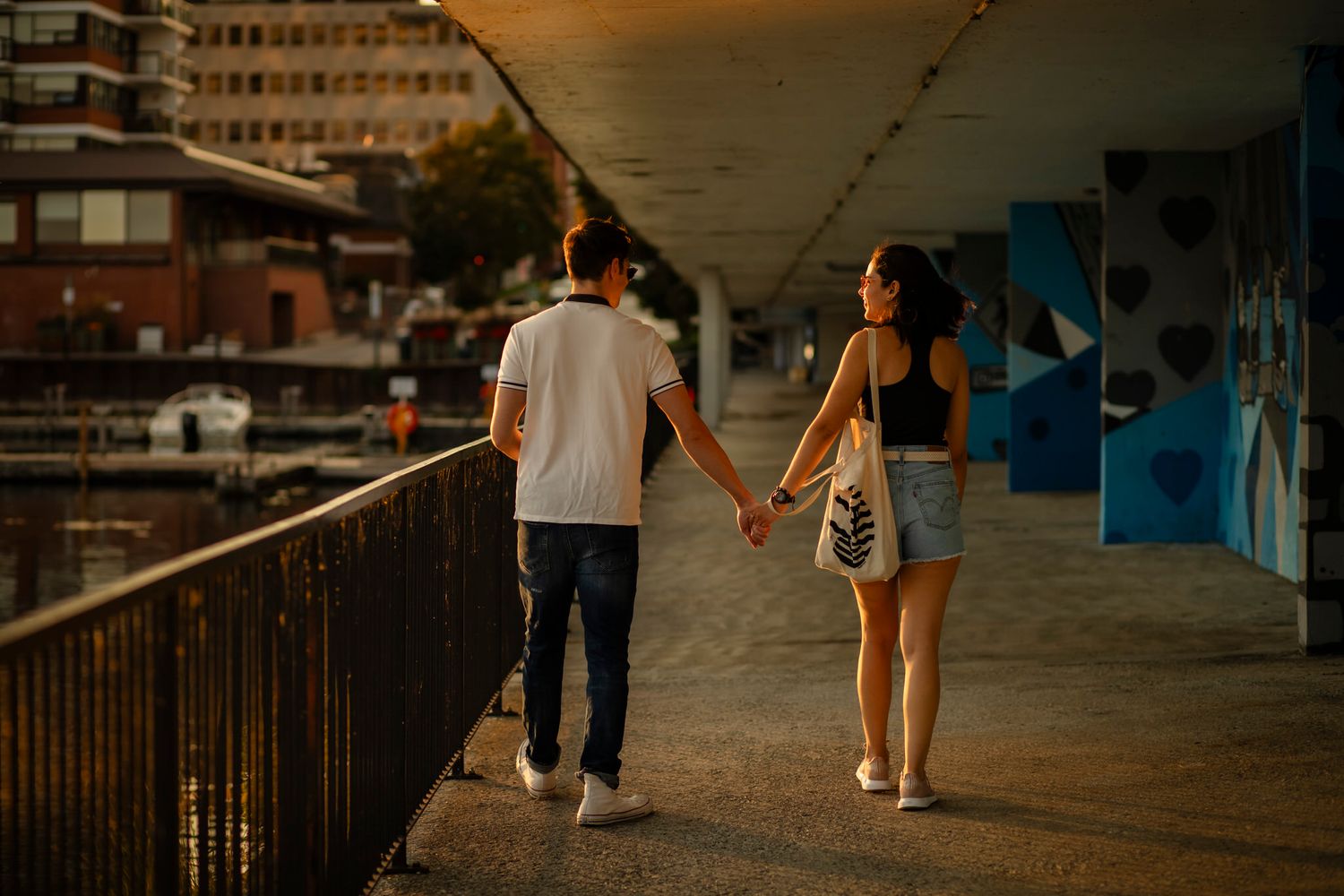 Couple walks along the boardwalk in the glowing, evening sun in downtown Kingston, Ontario, CA.