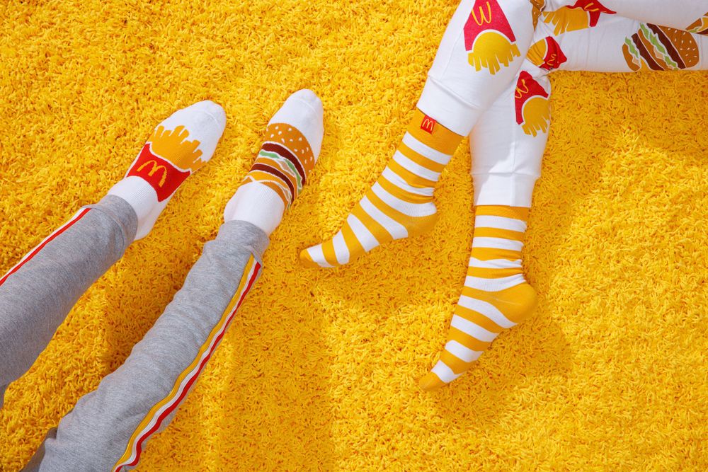 Legs wearing colorful striped socks and sneakers shown against a bright yellow carpet or rug background.