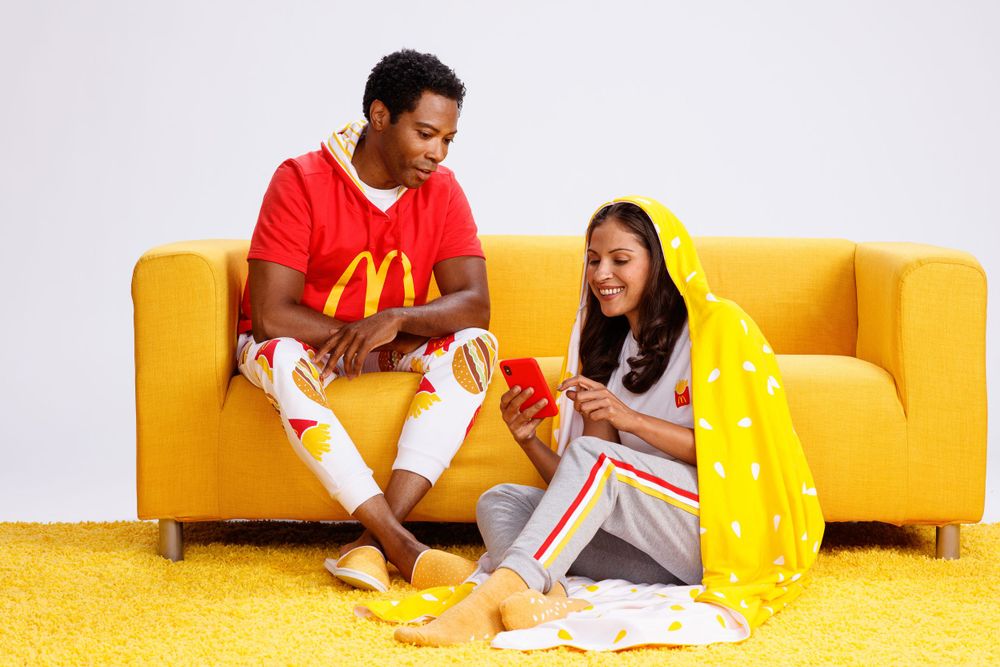 Two people enjoying McDonald's takeout food while sitting on a yellow couch against white wall.