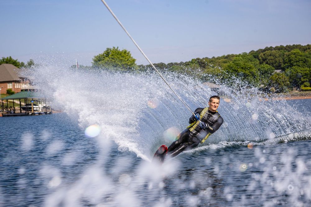 Man in wetsuit water skiing on a lake, creating a dramatic spray of water on a sunny day.